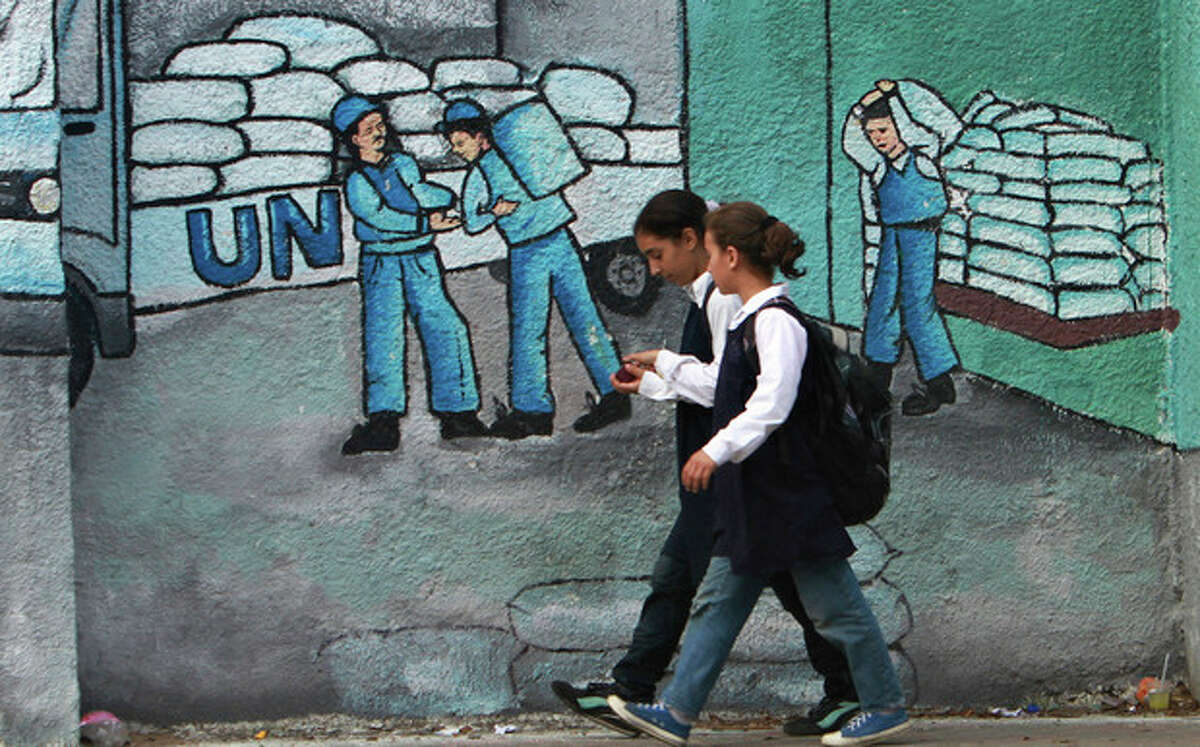 Palestinian school girls walk past a graffiti on a wall depicting UN humanitarian aid supplies, in Gaza City, Monday, Oct. 31, 2011. Palestine became a full member of the U.N. cultural and educational agency Monday, in a highly divisive move that the United States and other opponents say could harm renewed Mideast peace efforts. (AP Photo/Adel Hana)