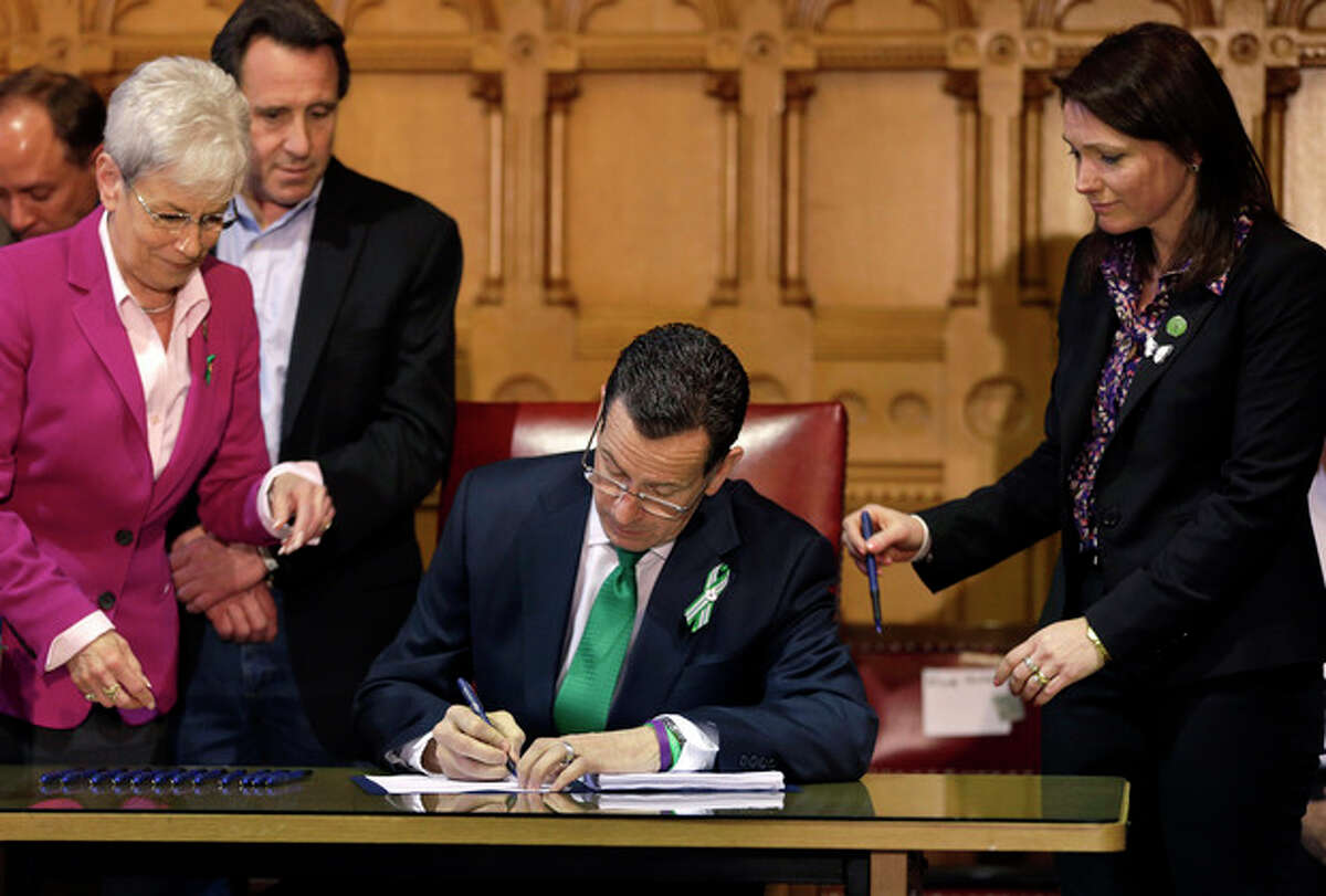 In this April 4, 2013, photo, Connecticut Gov. Dannel P. Malloy, center, signs legislation at the Capitol in Hartford, Conn., that includes new restrictions on weapons and large capacity ammunition magazines, a response to last year's deadly school shooting in Newtown. Neil Heslin, behind left, father of Sandy Hook shooting victim Jesse Lewis, Nicole Hockley, right, mother of Sandy Hook School shooting victim Dylan, and Conn. Lt. Gov. Nancy Wyman, left, watch. (AP Photo/Steven Senne)