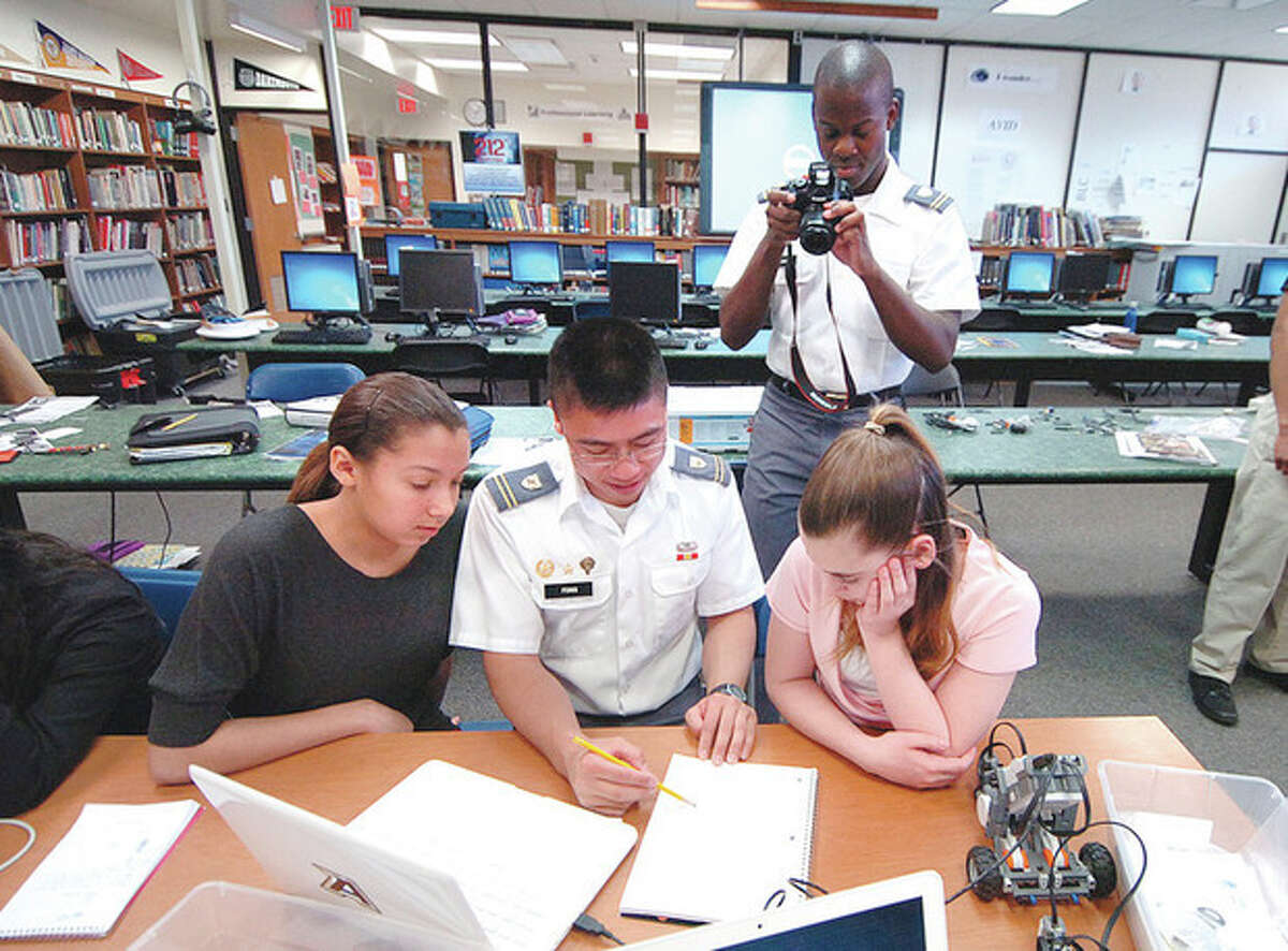 Hour Photo/Alex von Kleydorff . West Point Cadet Teddy Fong shows Esmerelda Rodriguez and Stephanie Melia how to input a program to make their robot complete a set course while Cadet Daniel Ford takes photos of the STEM program at Cloonan Middle School on Tuesday.