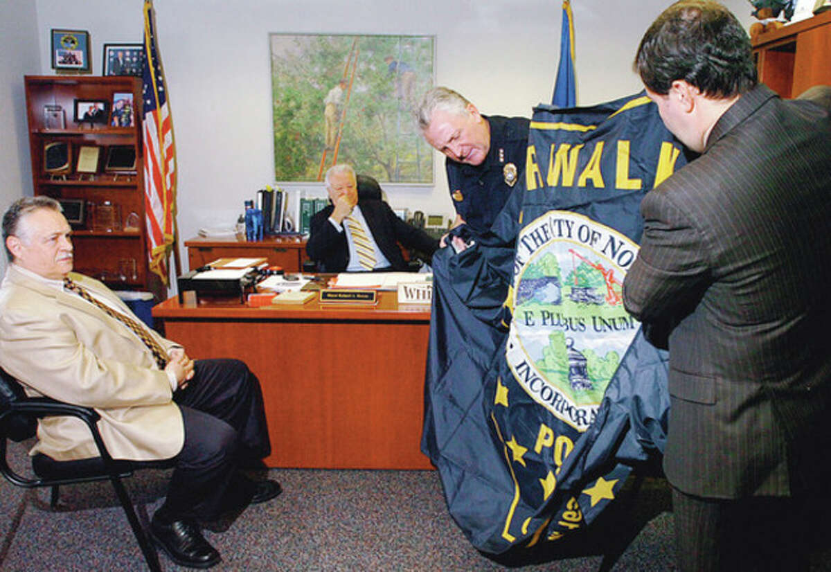 Hour photo / Erik Trautmann Norwalk Police Chief Harry Rilling and Police Union President Thomas Roncinske unfurl a flag for Police Commissioner Peter Torrano and Mayor Richard Moccia Thursday that Norwalk police officer and Army Reserve Sgt. Patrick English flew over the U.S. embassy when stationed in Iraq. See story Page A3.
