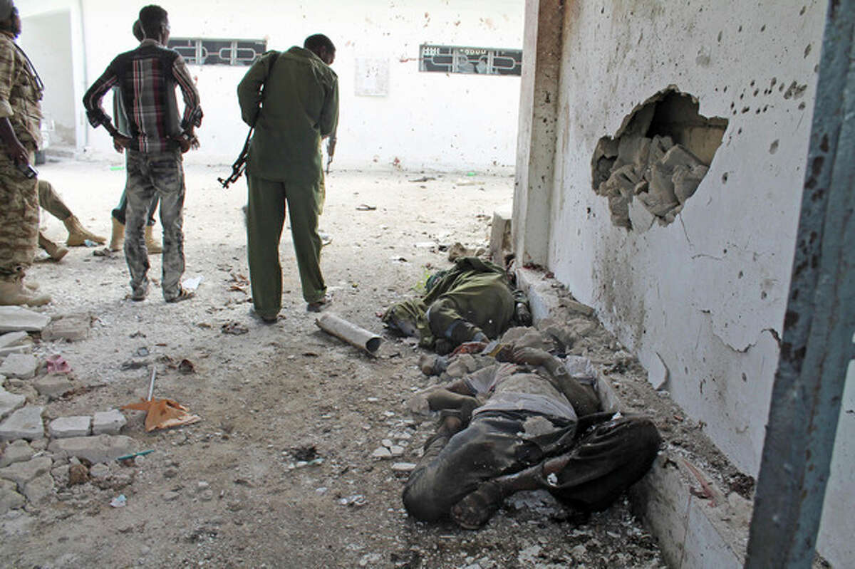 Somali soldiers stand over dead civilians lying at the entrance of Mogadishu?’s court complex after being killed during a siege by militants in Mogadishu, Somalia, Sunday, April 14, 2013. Militants launched a serious and sustained assault on Mogadishu's main court complex Sunday, detonating at least two blasts, taking an unknown number of hostages and exchanging extended volleys of gunfire with government security forces, witnesses said.(AP Photo/Farah Abdi Warsameh)