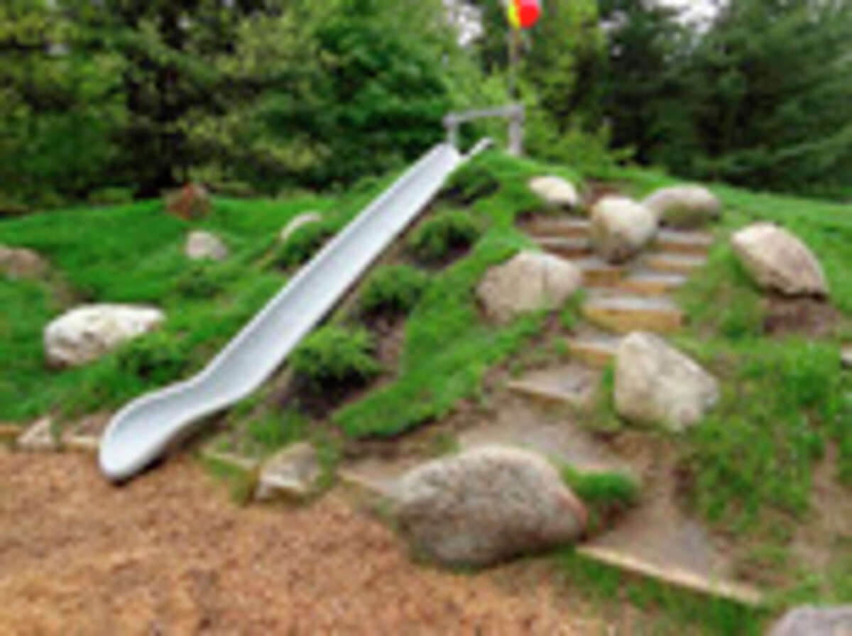 In this publicity photo provided by Natural Playgrounds Company, an embankment slide is built into a constructed hill at an elementary school as shown here in Glens Falls, N.Y. The embankment slide is safer than tower slides with ladders. Scattered boulders, random dirt steps, rough terrain, and varied plantings add to the rich textures and varied experiences on Natural Playgrounds. (AP Photo/Natural Playgrounds Company)