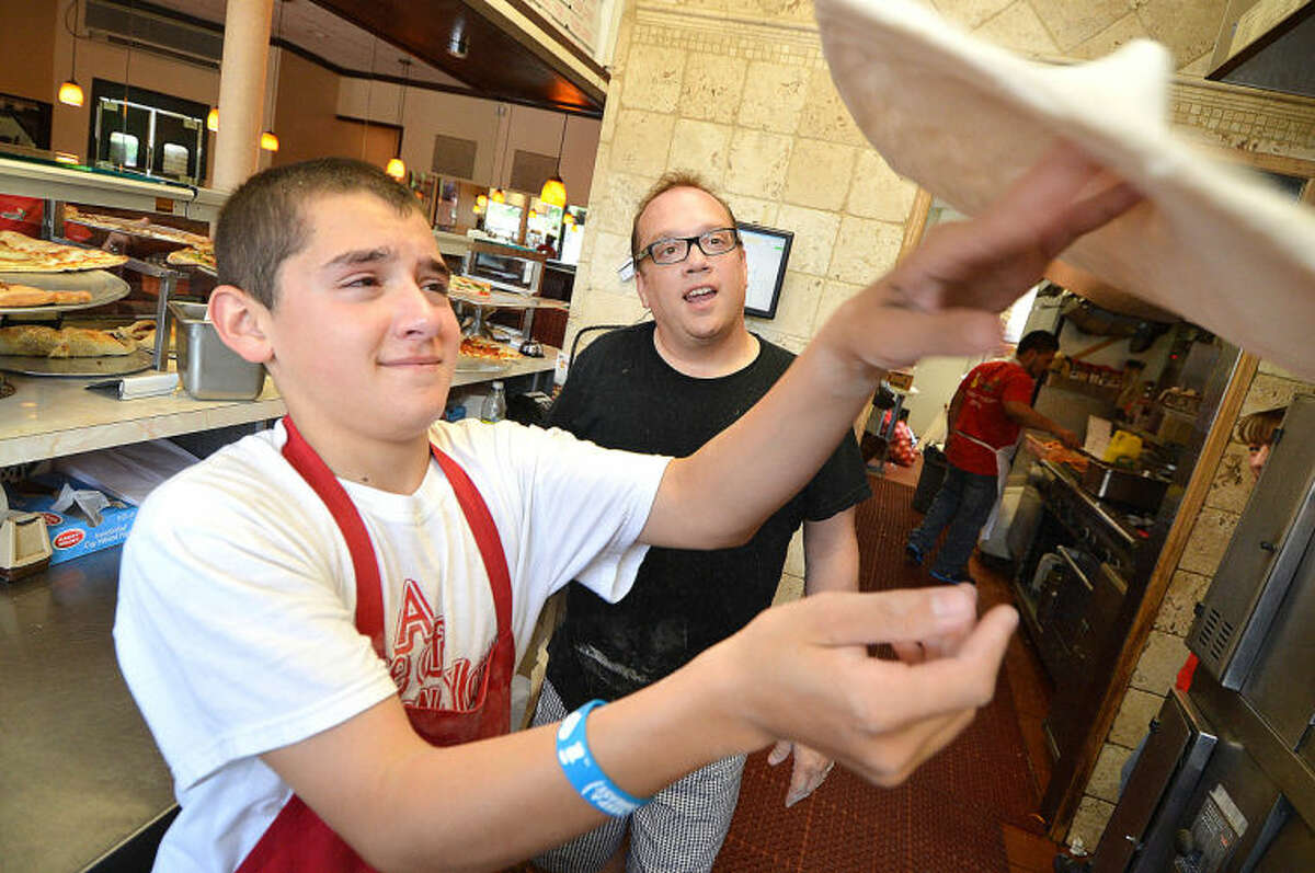 Hour Photo/Alex von Kleydorff World Champion, Master Pizzalolo and Pinocchio Pizza owner Bruno DiFabio watches as his 14 yr old son Anthony spins dough for a large Pulled Pork Pizza at his restaurant in Wilton center on Tuesday. All proceeds for the days sales go to The American Cancer Society to help in Cancer research.