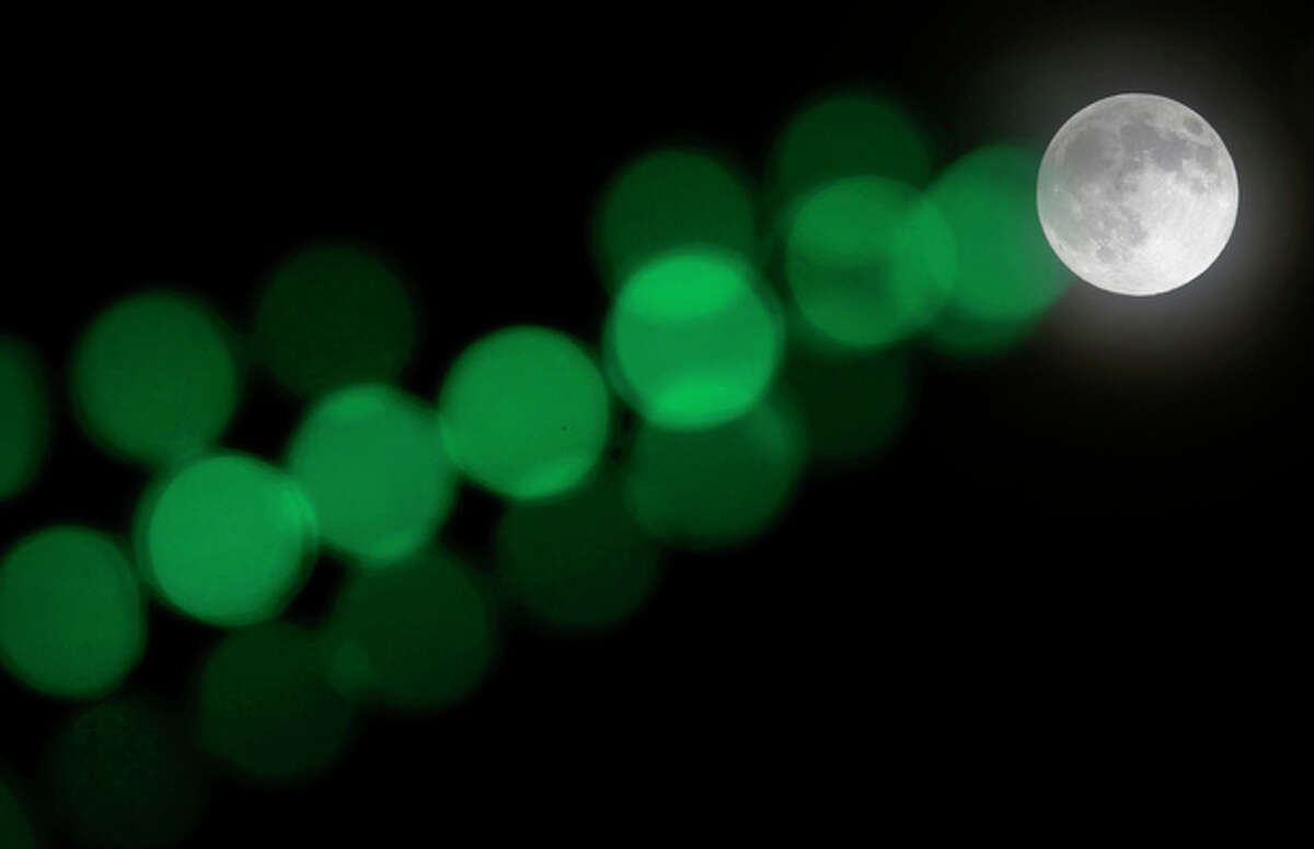A full moon rises through a hazy sky past a string of green lights, Saturday, June 22, 2013, in Baltimore. The moon, which will reach its full stage on Sunday, is expected to be 13.5 percent closer to earth during a phenomenon known as supermoon. (AP Photo/Patrick Semansky)