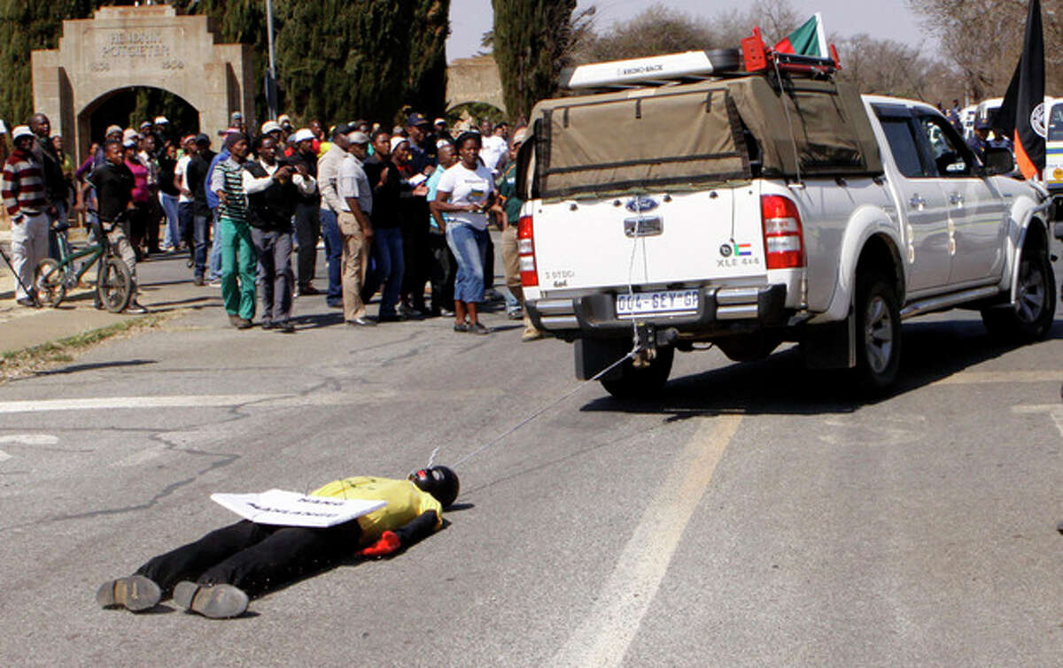 An effigy of the killer of right wing leader Eugene TerreBlanche is dragged behind a vehicle past protesters outside the court in Ventersdorp, South Africa, Wednesday Aug. 22 2012. A black farmworker was sentenced to life in prison Wednesday for the brutal murder of South African white supremacist leader Eugene Terreblanche in a case that has been a source of racial tension in the city of Ventersdorp. About 100 protesters sang anti-white songs outside the courtroom in the city just west of Johannesburg to support 30-year-old Chris Mahlangu, who had pleaded guilty but argued that he acted in self-defense in what the judge found was a violent dispute over wages. They were opposed by 20 white protesters who carried the doll of a black man with a rope around his neck and a sign that said: "Hang Mahlangu." (AP Photo/Denis Farrell)