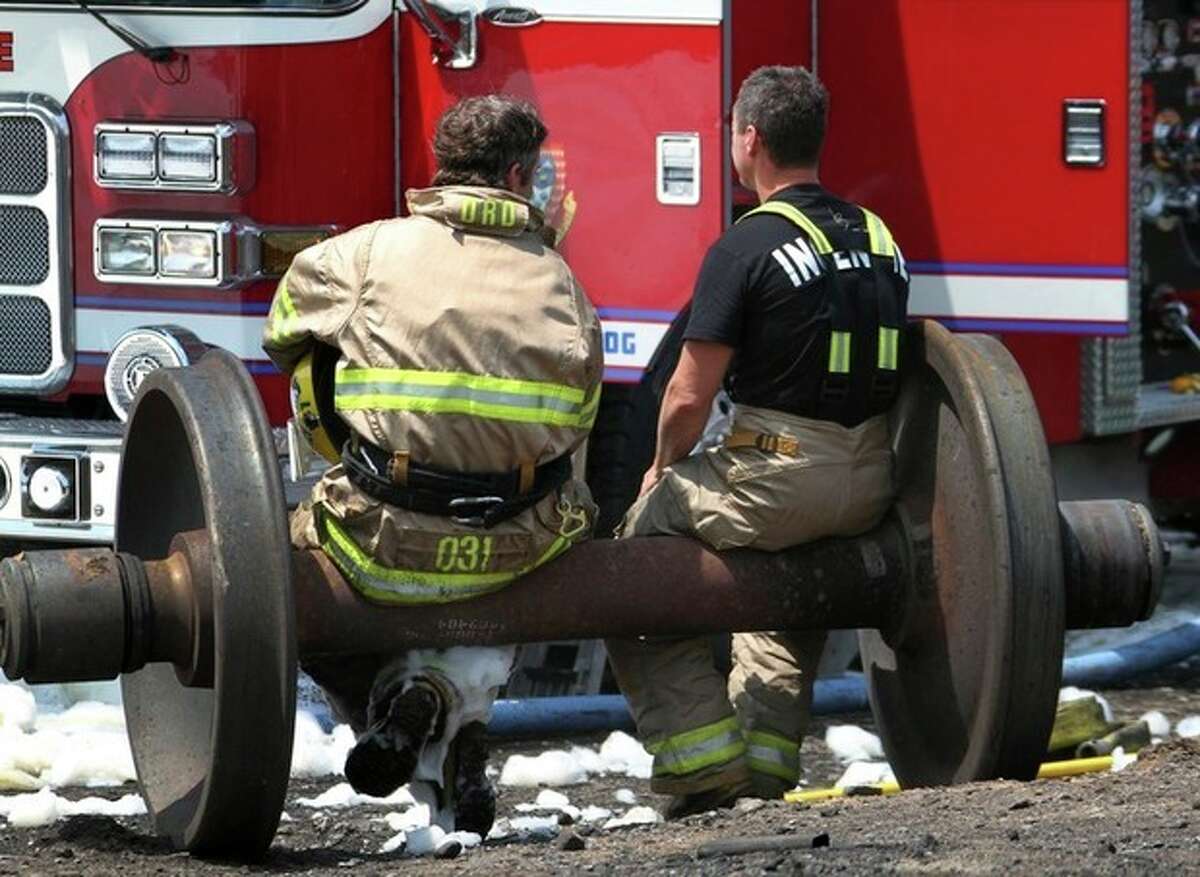 In a Sunday, July 7, 2013 photo, firefighters take a break on a set of train wheels in Lac-Megantic, Quebec, in a Surete du Quebec handout photo made available Tuesday, July 9, 2013. Thirteen people are confirmed dead and forty more are listed as missing after a train derailed ignited tanker cars carrying crude oil. (AP Photo/Surete du Quebec via The Canadian Press)