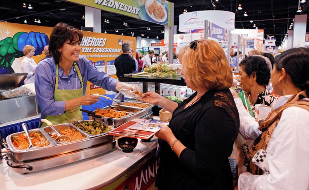 In this July 17, 2012 photo Diane Wagner, with Schwan Food Co., hands out samples of food at a booth during the School Nutrition Association conference in Denver. There are plenty of vegetables and other healthy options on school menus these days. The challenge is getting children to eat them. (AP Photo/Ed Andrieski)