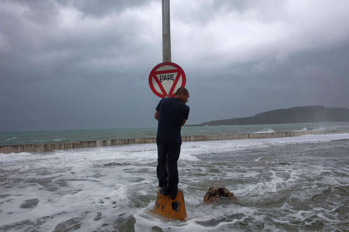 A man stands on a post with a stop sign as waves pass the seawall during the passage of Tropical Storm Isaac in Baracoa, Cuba, Saturday, Aug. 25, 2012. Tropical Storm Isaac pushed into Cuba on Saturday after sweeping across Haiti's southern peninsula. Isaac's center made landfall just before midday near the far-eastern tip of Cuba. (AP Photo/Ramon Espinosa)