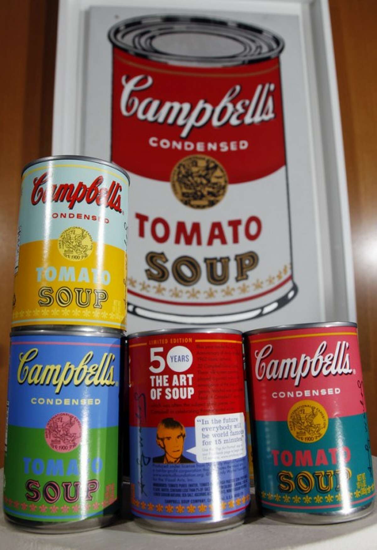 In this photograph taken Aug. 24, 2012, new limited edition Campbell's tomato soup cans with art and sayings by artist Andy Warhol are displayed in front of an original Warhol Pop Art painting from the 1960's in the boardroom at Campbell Soup Company in Camden, N.J. Campbell plans to introduce the special-edition cans of its condensed tomato soup bearing labels reminiscent of the pop artist's paintings at Target stores starting Sunday, Sept. 2, 2012. (Photo/Mel Evans)