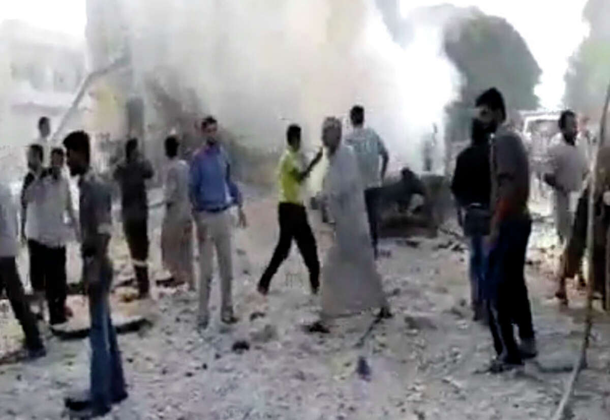 In this image made from amateur video released by the Shaam News Network and accessed Tuesday, Aug. 28, 2012, Syrian men stand near smoke rising from buildings due to shelling in Kfarnebel, Idlib province, northern Syria. (AP Photo/Shaam News Network via AP video) THE ASSOCIATED PRESS IS UNABLE TO INDEPENDENTLY VERIFY THE AUTHENTICITY, CONTENT, LOCATION OR DATE OF THIS HANDOUT PHOTO