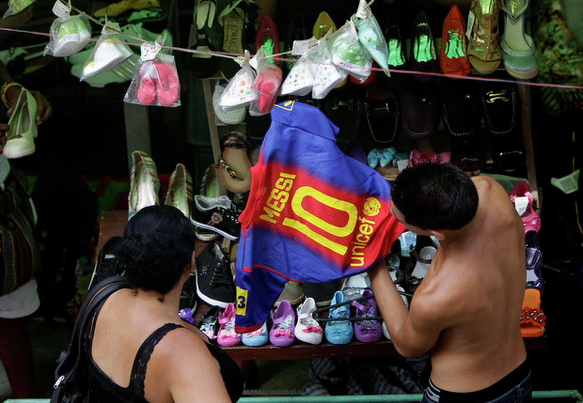A shopper looks at a copy of a FC Barcelona soccer team shirt with the name of player Lionel Messi at an outdoor market where the government allows licensed vendors to sell their goods in downtown Havana, Cuba, Friday, Aug. 31, 2012. A jump in import taxes on Monday, Sept. 3 threatens to make life tougher for some of Cuba's new entrepreneurs who the government has been trying to encourage as it cuts a bloated workforce in the socialist economy. In Cuba, the average monthly wage is about $20. (AP Photo/Franklin Reyes)