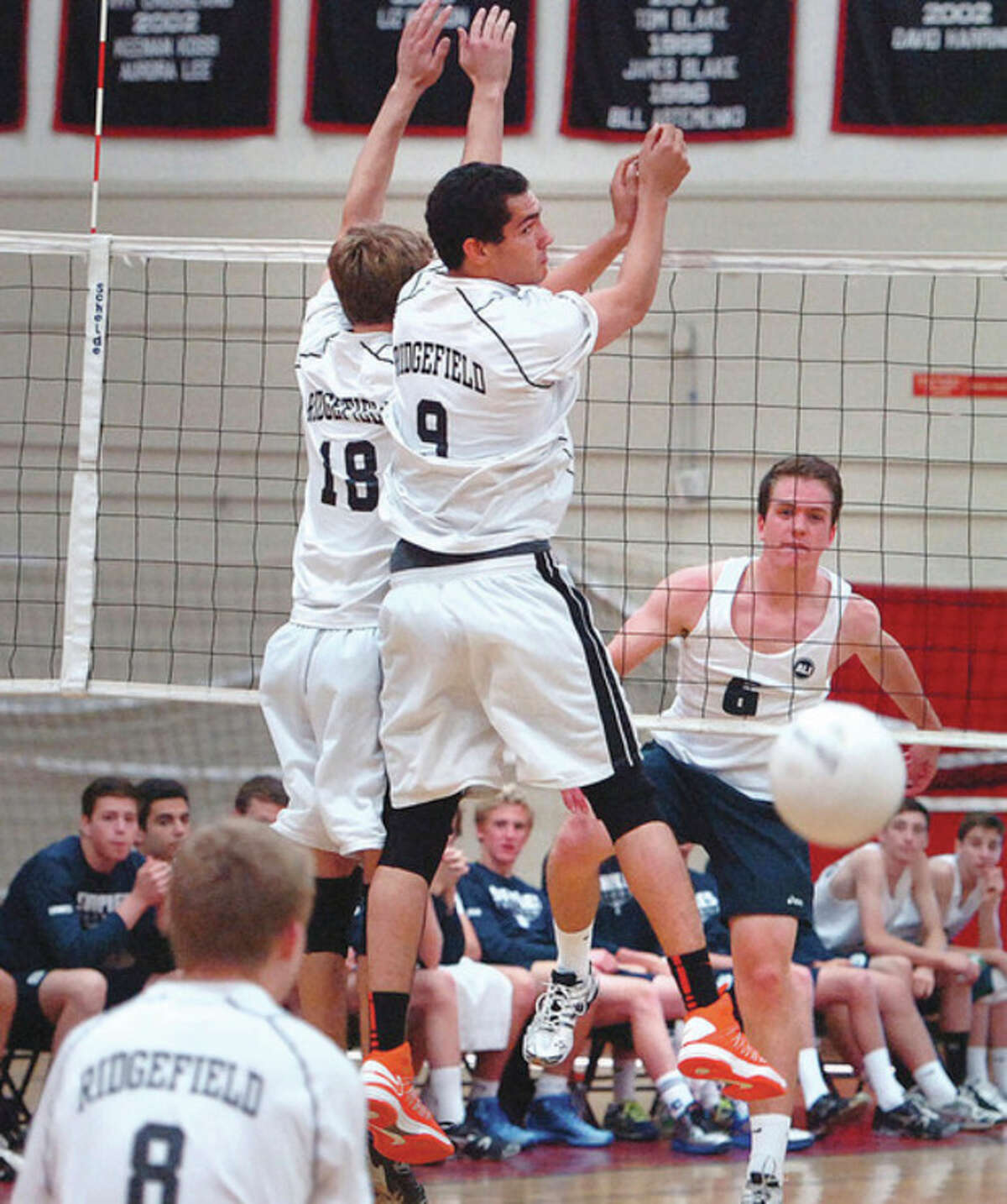 Hour photo/Alex von Kleydorff Ryan Petyerson of Staples, right, pounds home a point past Ridgefield's Tyler Chittenden (18) and Griffin Jones during Tuesday's CIAC Class L volleyball state semifinal match. A 3-0 win put Staples in Friday's final.