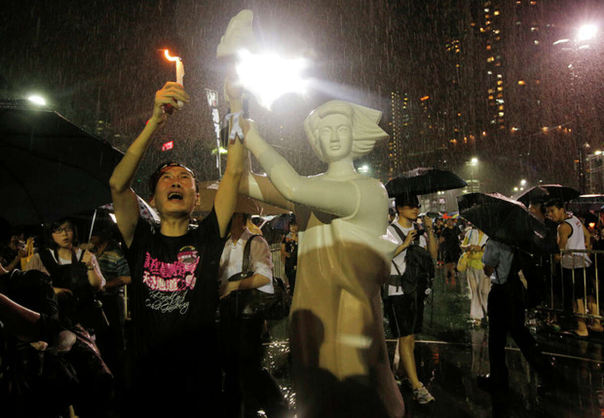 A man holds candlelight in front of a replica of the Goddess of Democracy as tens of thousands of people attend a candlelight vigil under heavy rain at Victoria Park in Hong Kong Tuesday June 4, 2013 to mark the 24th anniversary of the June 4th Chinese military crackdown on the pro-democracy movement in Beijing. (AP Photo/Vincent Yu)