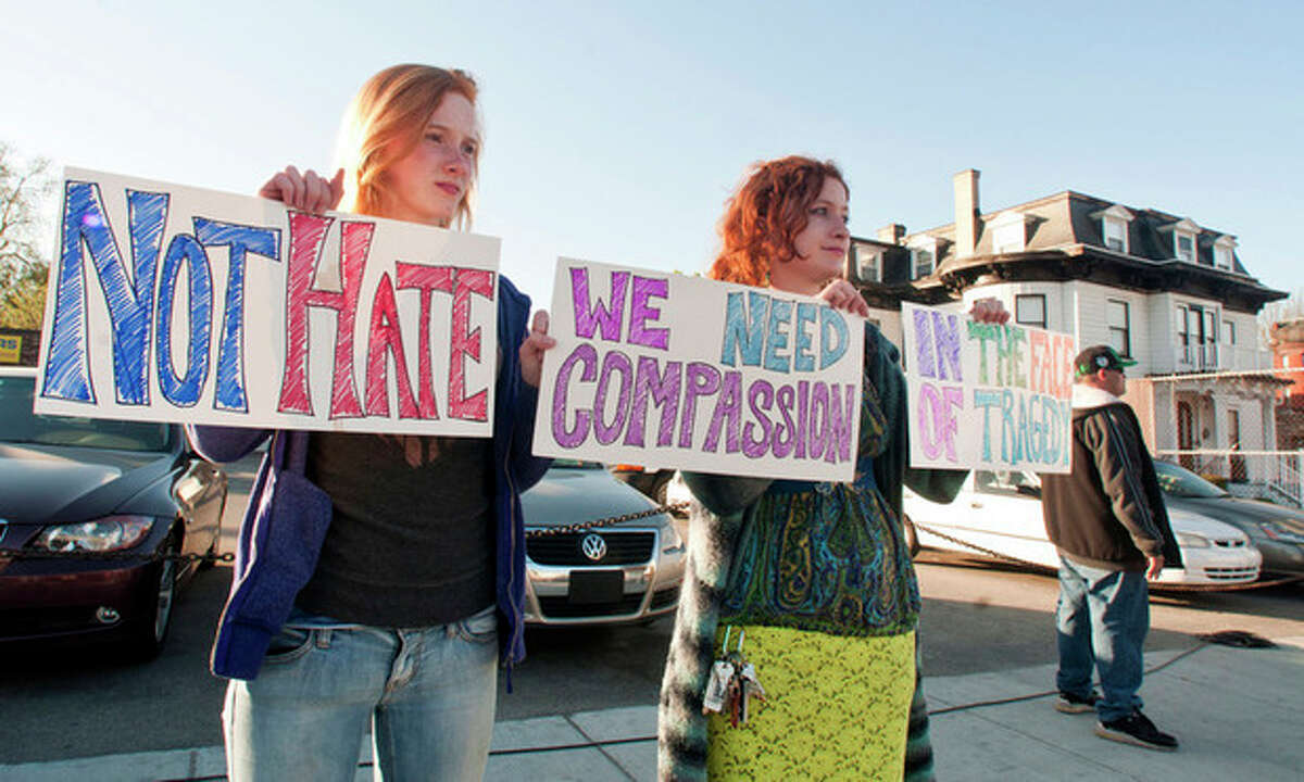 Fiona Gilley, left, and her sister Nairi Melkonian, both of Worcester, Mass., hold signs urging compassion while they stand on the other side of the street from protestors on Sunday evening, May 5, 2013 in Worcester, Mass. Boston marathon bombing suspect Tamerlan Tsarnaev's body is being held at Graham Putnam & Mahoney Funeral Parlors on Main Street in Worcester, the building at right, until a cemetery can be found that will accept the body for burial. (AP Photo/Worcester Telegram & Gazette, Betty Jenewin)
