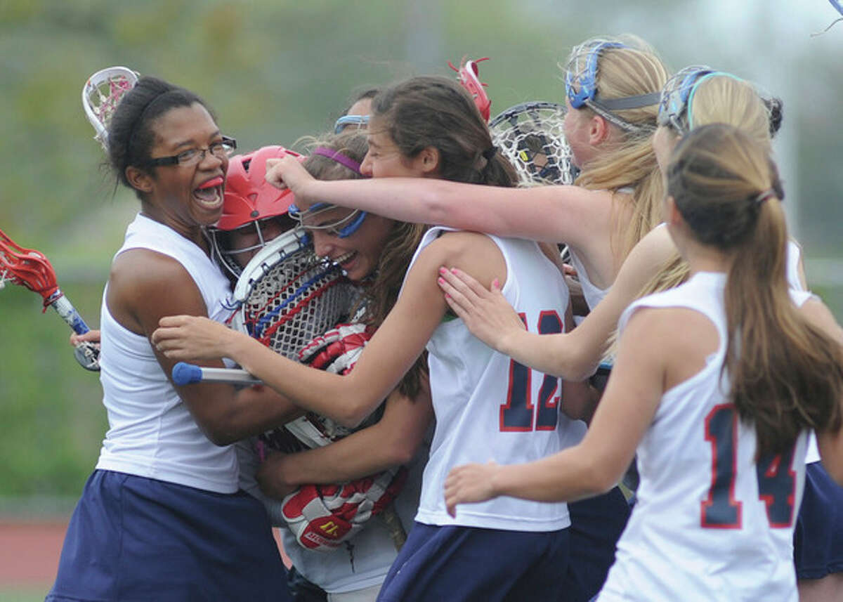 Hour photo/John Nash Brien McMahon girls lacrosse goalie Michele Petrucci, second from left in red helmet, is mobbed by teammates, including senior Gabbie Robinson, left, after backstopping McMahon's 12-6 win over Bunnell on Saturday. The win snapped a 29-game losing streak by McMahon.