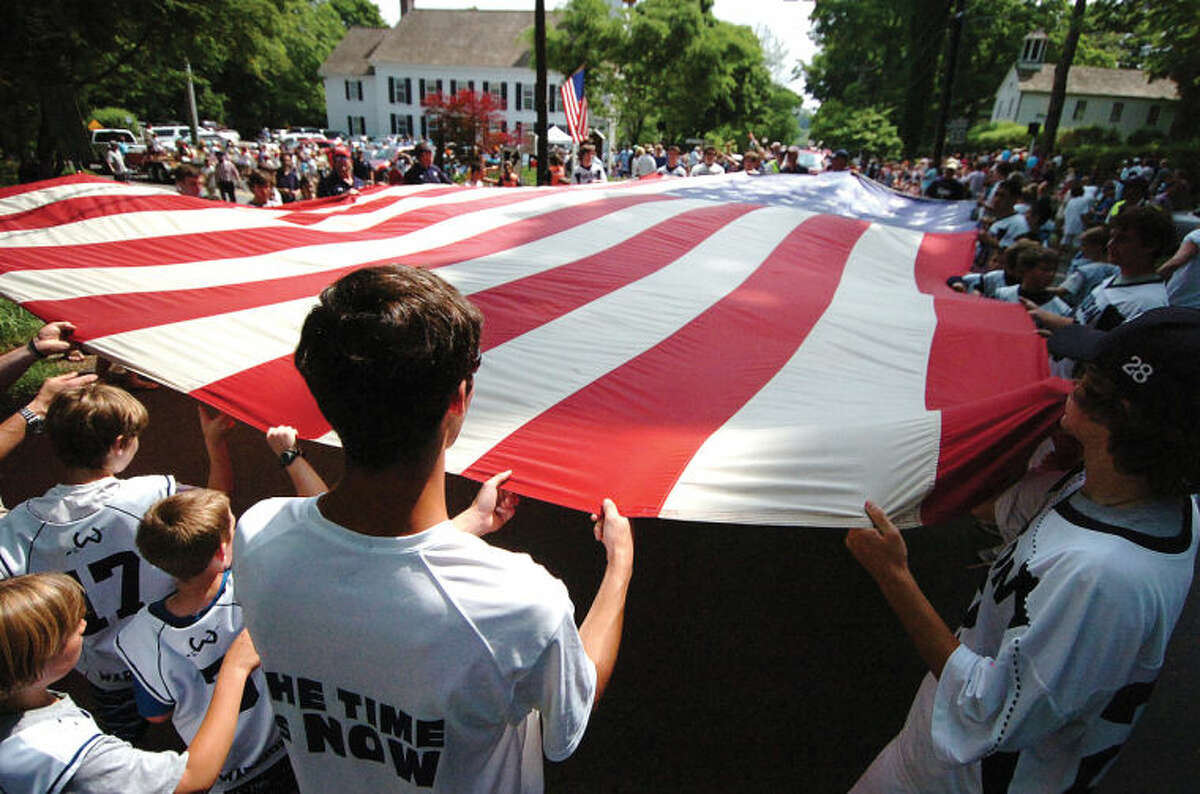 Hour Photo/ Alex von Kleydorff. Wiltons Lacrosse teams carry a giant American Flag past the Congregational Church during Wiltons Memorial Day Parade.