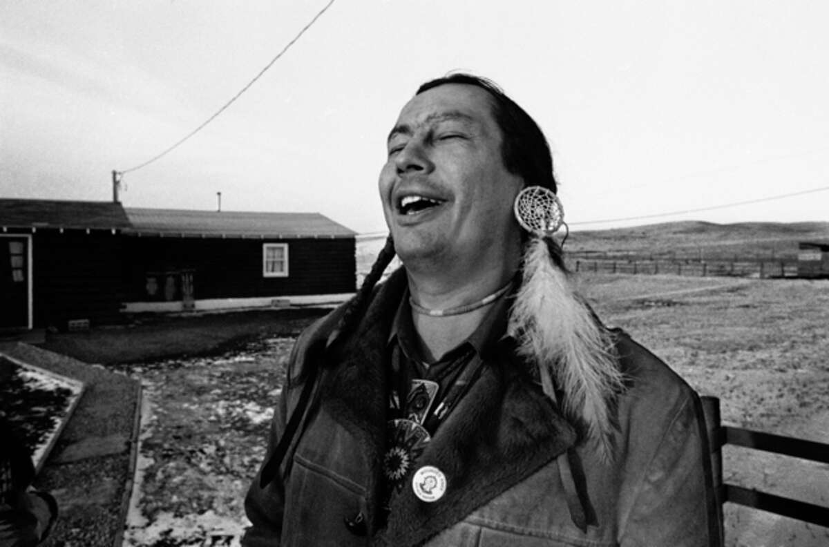 FILE - In a Feb. 4, 1974 file photo, American Indian Movement (AIM) leader Russell Means, who is challenging incumbent Oglala Sioux Tribal President Richard Wilson in Thursday's election on the Pine Ridge Indian Reservation, laughs at news report which quoted Wilson as saying he will give AIM 10 days to get off the reservation after he is reelected "or else", in Pine Ridge, S.D. Means, a former American Indian Movement activist who helped lead the 1973 uprising at Wounded Knee, reveled in stirring up attention and appeared in several Hollywood films, died early Monday, Oct. 22, 2012 at his ranch in in Porcupine, S.D., Oglala Sioux Tribe spokeswoman Donna Solomon said. He was 72. (AP Photo/Jim Mone, File)