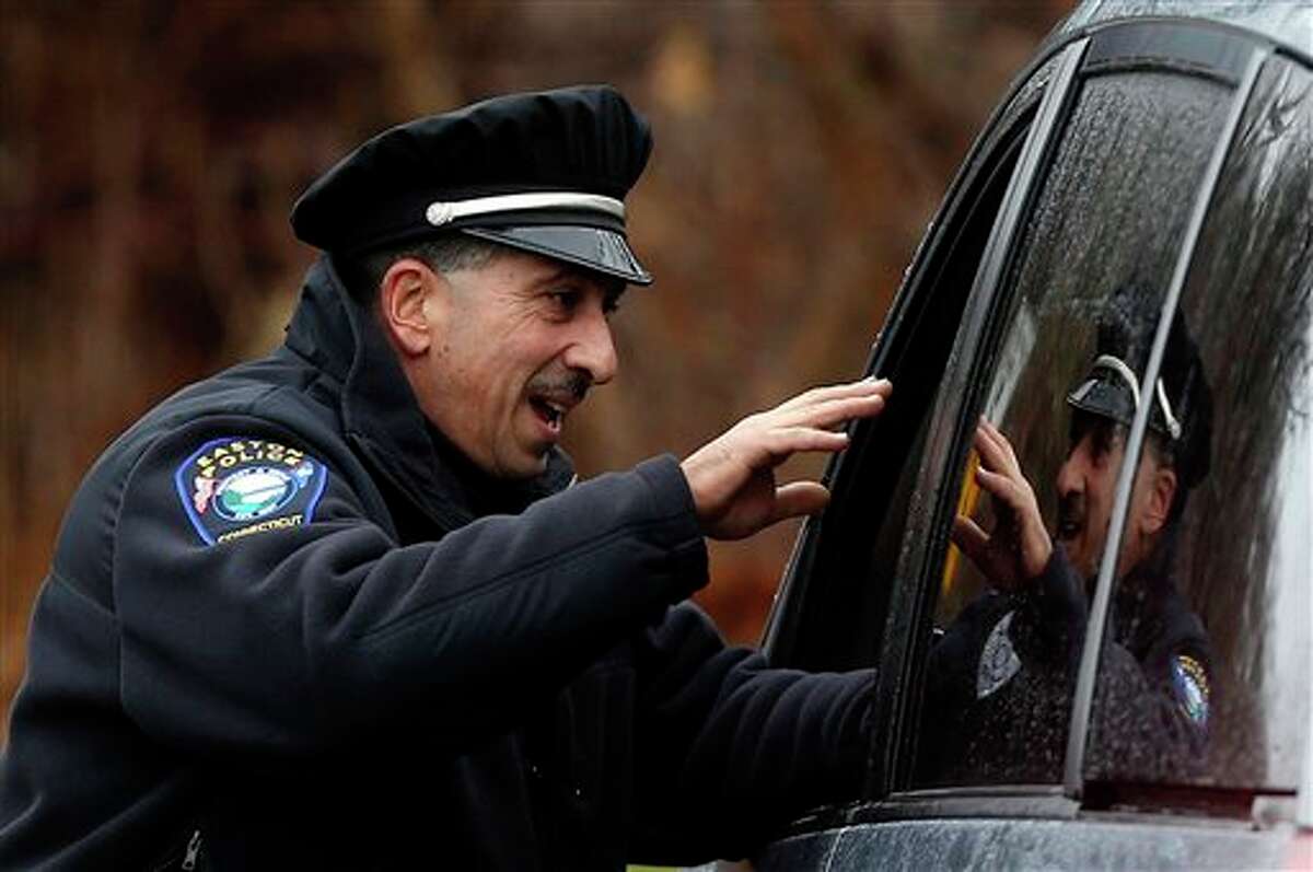 Easton police officer J. Sollazzo waves to a returning student as a car pulls into Hawley School, Tuesday, Dec. 18, 2012, in Newtown, Conn. Classes resume Tuesday for Newtown schools except those at Sandy Hook. Buses ferrying students to schools were festooned with large green and white ribbons on the front grills, the colors of Sandy Hook. At Newtown High School, students in sweatshirts and jackets, many wearing headphones, betrayed mixed emotions. Adam Lanza walked into Sandy Hook Elementary School in Newtown, Friday and opened fire, killing 26 people, including 20 children, before killing himself.(AP Photo/Jason DeCrow)