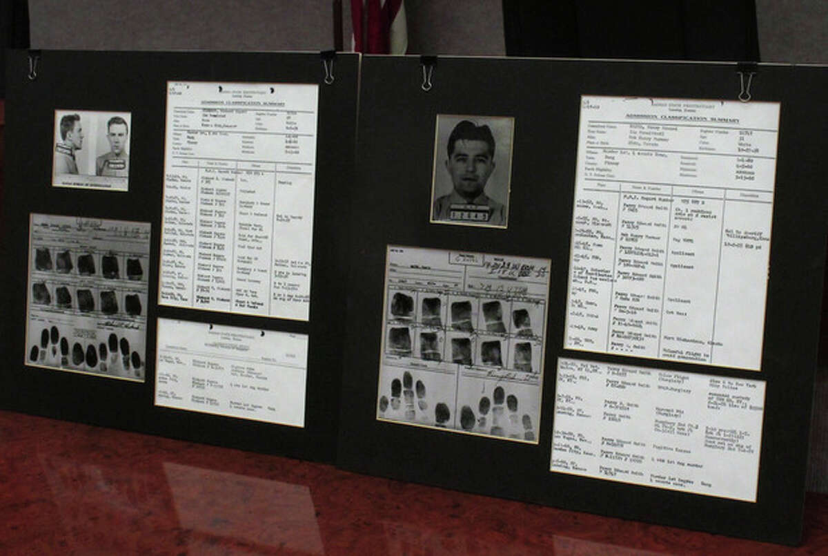 This photo from Tuesday, Dec. 18, 2012, shows a display of prison records for Richard Hickock, left, and Perry Smith, used at a news conference in Lansing, Kan. The two men were executed for the 1959 multiple murders that inspired Truman Capote's book, "In Cold Blood," and their remains have been exhumed and reburied so that authorities could collect DNA samples as possible evidence linking them to Florida killings. (AP Photo/John Hanna)