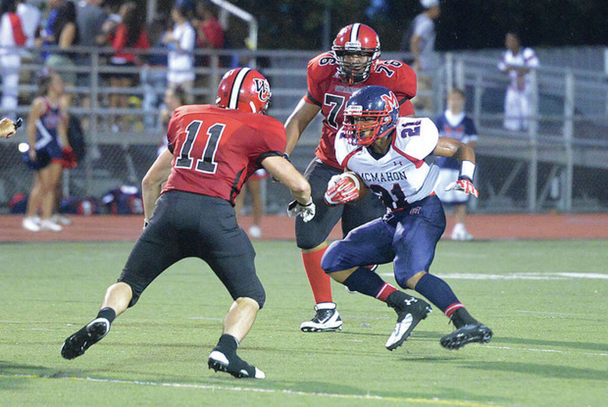 Hour Photo/Alex von Kleydorff Brien McMahon's Timmy Hinton (21) looks for running room after making a catch as Wilbur Cross defender Jake Mahoney defends the play during Thursday's season-opening football game in Norwalk. Hinton turned the reception into a 66-yard touchdown play, giving McMahon at 13-0 lead, but soon the rains and lightning game forcing a suspension of the game.