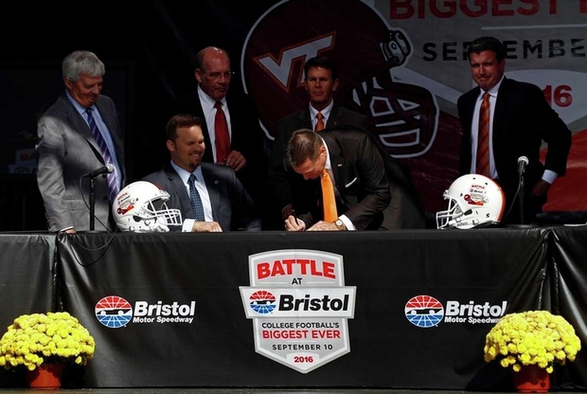 Tennessee head football coach Butch Jones signs the contract as Marcus Smith, president of Speedway Motorsports, seated, Virginia Tech head football coach Frank Beamer, standing at left, Virginia Tech athletic director Jim Weaver, second from left, Tennessee athletic director Dave Hart, second from right, and Jerry Caldwell, general manager of Bristol Motor Speedway, right, watch during a press conference at Bristol Motor Speedway Monday, Oct. 14, 2013, in Bristol, Tenn. Tennessee and Virginia Tech will finally play a football game at Bristol Motor Speedway in what is being billed as the "Battle of Bristol." (AP Photo/Wade Payne)
