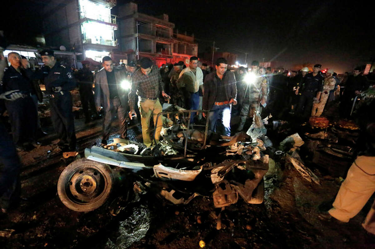 Civilians and security forces inspect the site of a double car bomb attack at a vegetable market in the Shiite holy city of Najaf, 100 miles (160 kilometers) south of Baghdad, Iraq, Thursday, Nov. 28, 2013. Officials in Iraq say attacks across Iraq killed tens of people Thursday. (AP Photo/Jaber al-Helo)