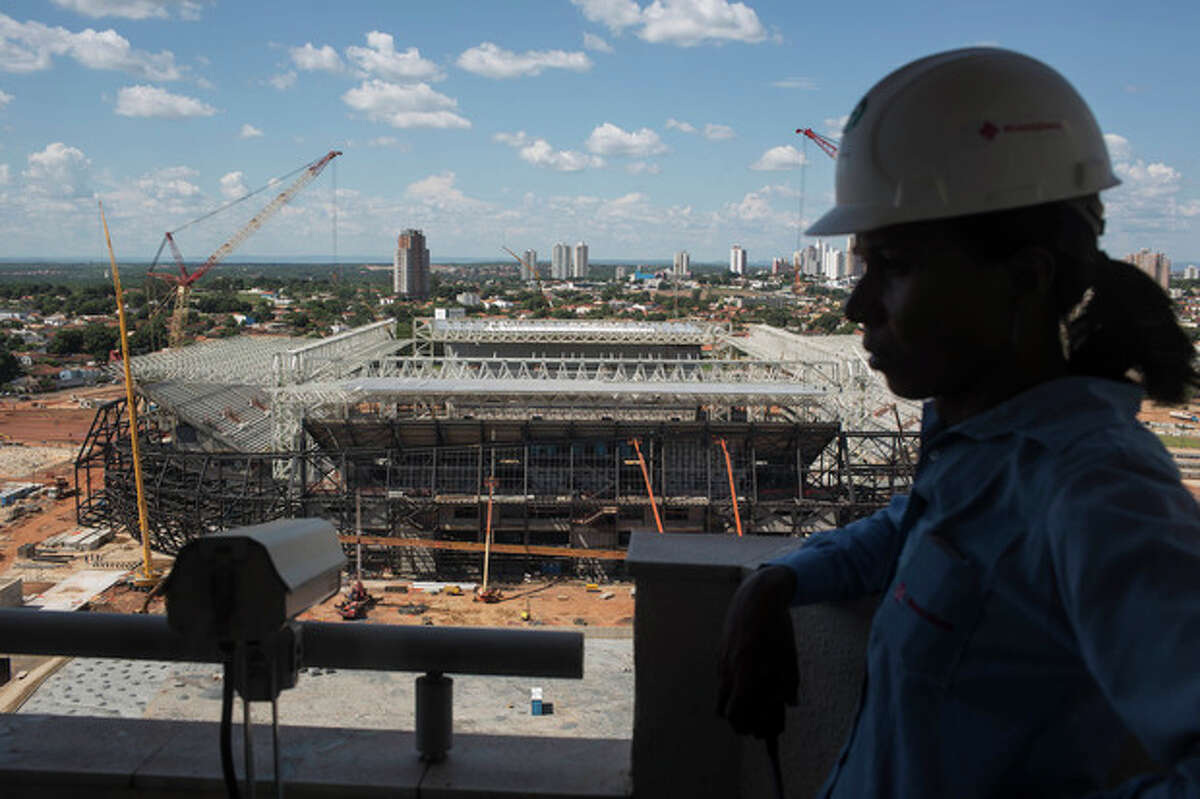 FILE .- In this Thursday Nov. 14, 2013 file photo, a worker stands next to a camera used to monitor the construction of the Arena Pantanal stadium that will host games during the 2014 World Cup soccer tournament in Cuiaba, Brazil. There is an ongoing court battle over the supplier of seats for the Arena Pantanal, meaning at any moment a judge can stop construction. From the moment a crane dramatically collapsed at the Sao Paulo stadium, it was clear World Cup organizers would have their hands full trying to deliver all 12 venues by FIFA's end-of-December deadline.(AP Photo/Felipe Dana, File)