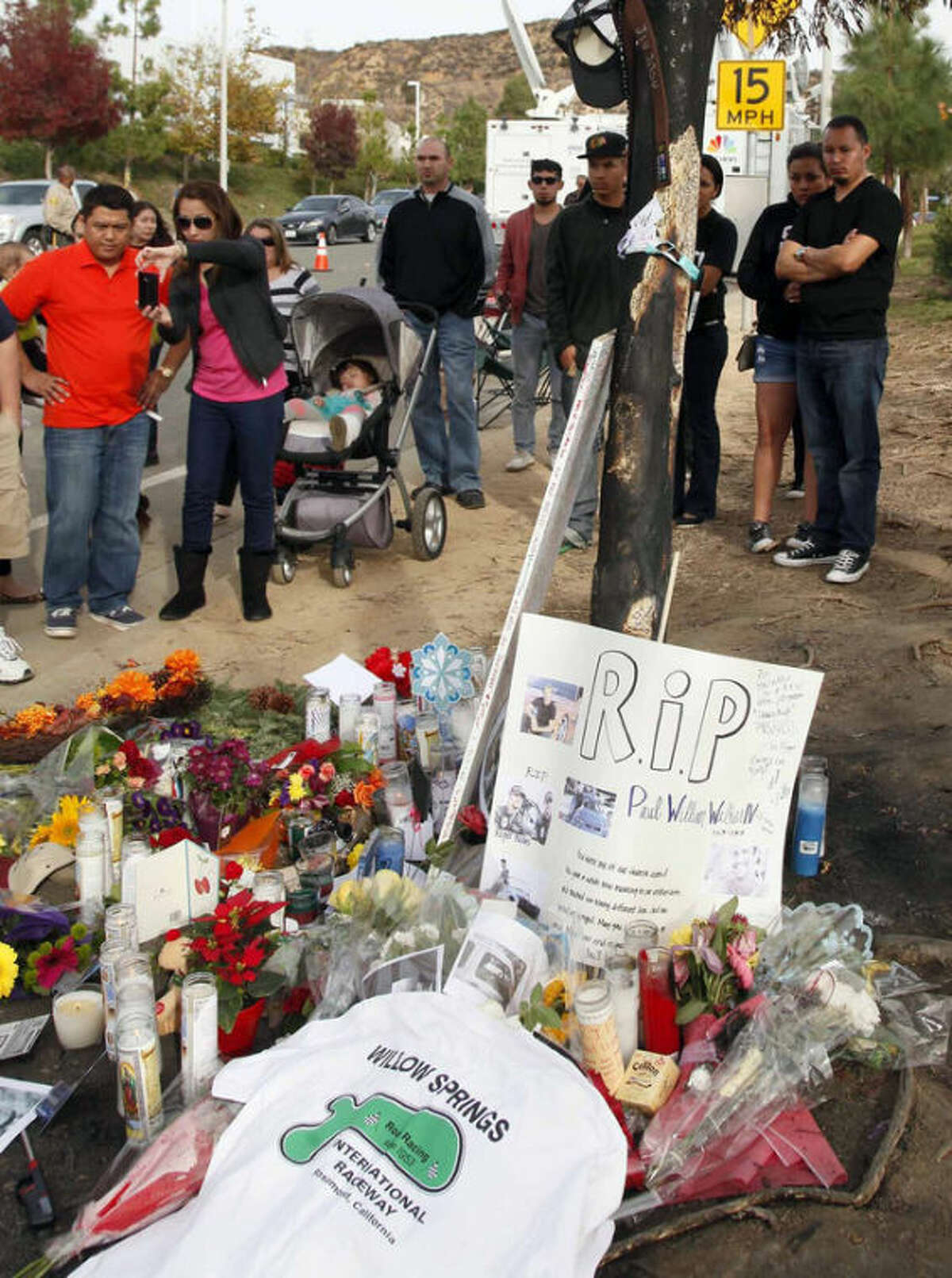People view a roadside memorial at the site of the auto crash that took the life of actor Paul Walker and another man, in the small community of Valencia, Calif., Monday, Dec. 2, 2013. The neighborhood where "Fast & Furious" star Walker died in the one-car crash is known to attract street racers, according to law enforcement officials. Walker and his friend and fellow fast-car enthusiast Roger Rodas died Saturday when the 2005 Porsche Carrera GT they were traveling in smashed into a light pole and tree. The two had taken what was expected to be a brief drive away from a charity fundraiser at Rodas' custom car shop in Valencia, about 30 miles (48 kilometers) northwest of Los Angeles. (AP Photo/Nick Ut)