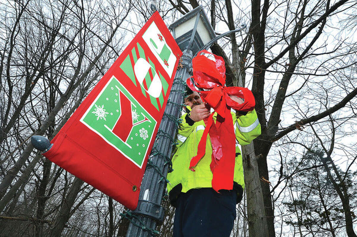 Photo by Alex von Kleydorff Bruno Mignogna of Wilton Parks & Recreation places a red bow on a lamp post after setting the Joy banner and a string of lights on one of the lampposts in Wilton Center on Monday.