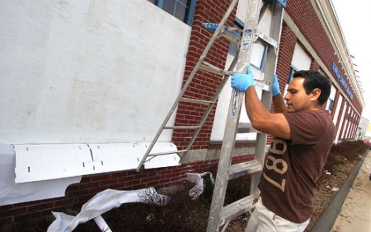 Photo/Alex von Kleydorff. Cesar Barroz, Facility Manger for the Norwalk Community Health center on Water St. Moves his ladder to the next panel where he has placed plywood over the windows and is in the process of painting them all white. The center has been burglarized more than once.