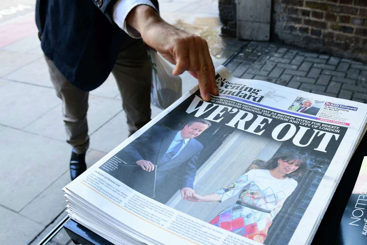 A man takes a copy of the London Evening Standard with the front page reporting the resignation of British Prime Minister David Cameron and the vote to leave the EU, a decision affecting stock prices globally.