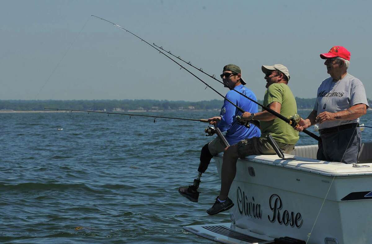 Sergio Cano of Seymour, Conn, a wounded combat veteran looks over as his father Walter Cano, center, attempts to hook a strike while fishing with Joseph Santagata on the Long Island Sound off of Stamford, Connecticut. The group was participating in the Hooks for Heroes Charity Fishing Tournament, hosted by the Halloween Yacht Club in Stamford, Conn. on Saturday, June 25, 2016. The event brought together area Veterans and several injured Vets from the Walter Reed Army Hospital for a day of fishing on the Long Island Sound. Several thousands of dollars were raised to help benefit Operation Gift Cards, one of several charity's supporting combat wounded vets.