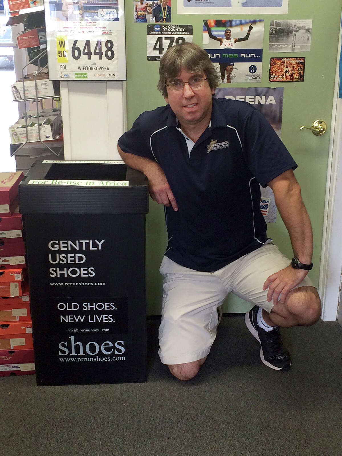 Chris Dickinson of Woodbridge Running Company kneels by one of the collection boxes for old shoes to be donated the Rerun Shoes program.