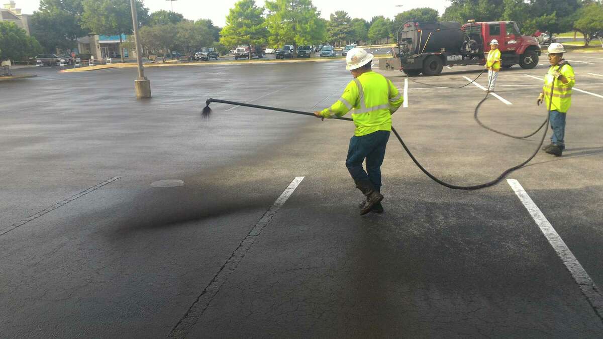 Workers in Austin apply an asphalt emulsion seal-coating product to a parking lot. This product would still be allowed under a proposed San Antonio ordinance that would ban sealants made from coal tar.