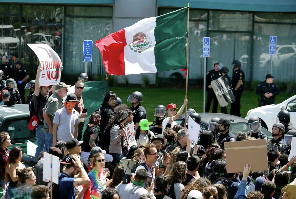 File - In this April 29, 2016, file photo, a protester against Republican presidential candidate Donald Trump waves a flag of Mexico outside of the Hyatt Regency hotel where the California Republican Party 2016 Convention is taking place in Burlingame, Calif., Friday, April 29, 2016. It's a flag seen at many protests against presumptive Republican presidential nominee Donald Trump. It also can be spotted at immigration rallies, on murals in cities with sizable Latino populations and at Mexican National team soccer games held on U.S. soil. The flag of Mexico has a long history in the United States, despite being a symbol of a nation south of the border. (AP Photo/Eric Risberg, File)