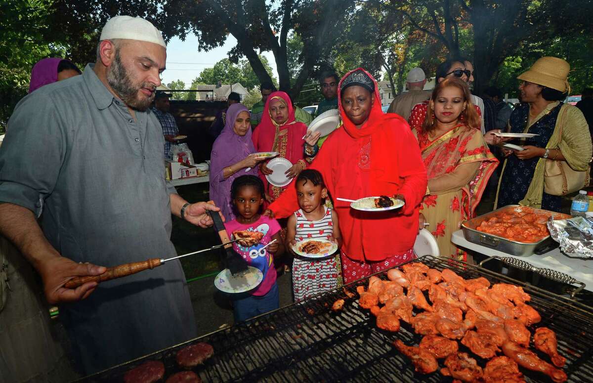 Faruk Vahora serves chicken to Taaraa Muhammad and her grandaughters, Essence Makeba and Se'nyah Watson, both 4, as The Al Madany Islamic Center of Norwalk celebrates the end of Ramadan on Wednesday with a community BBQ at the mosque, One Union Park.