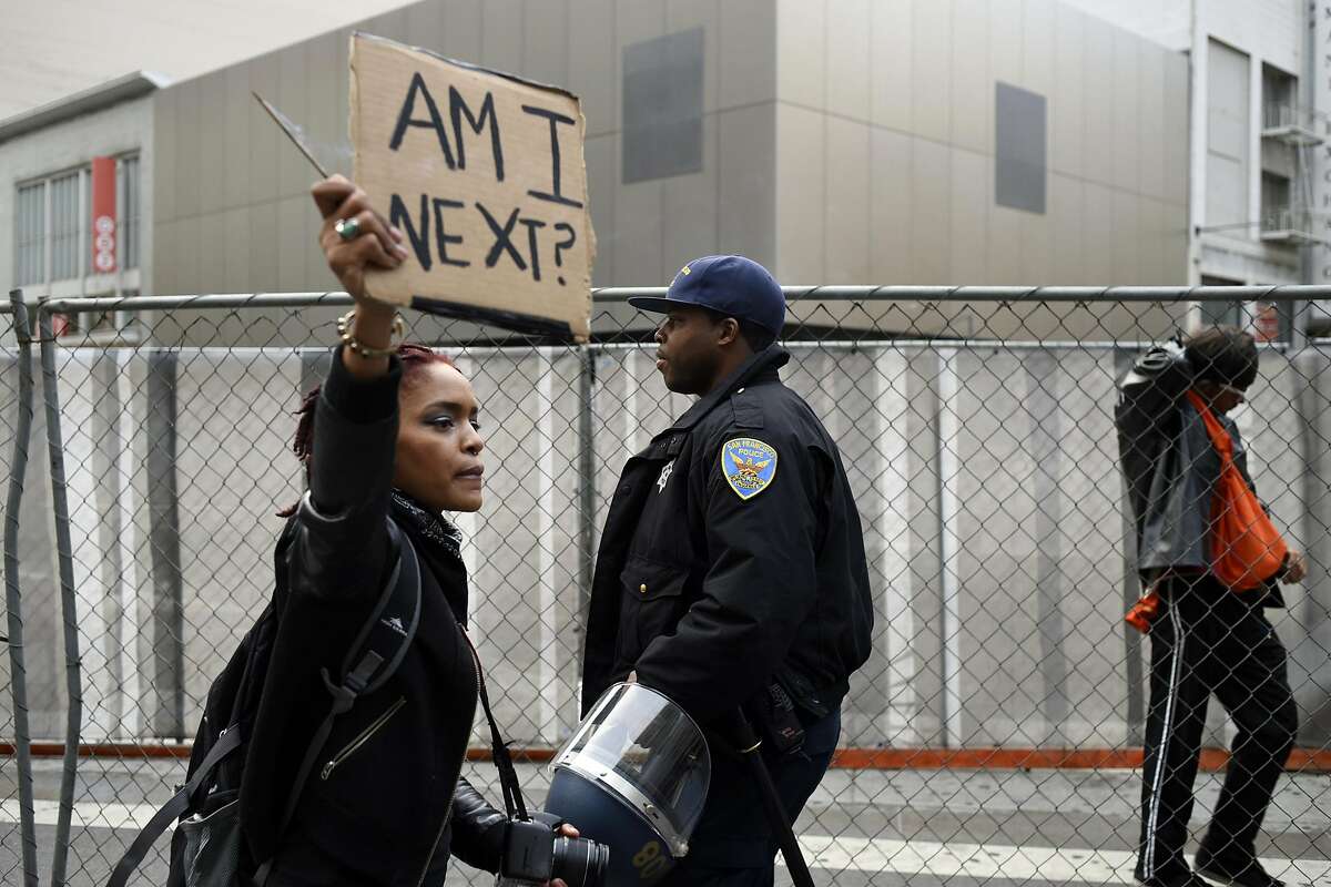 A woman who declined to give her name holds a sign near a police officer as protestors march down Market St. in San Francisco, Calif., on Friday, July 8, 2016, to protest against recent police shootings in Minnesota and Louisiana.