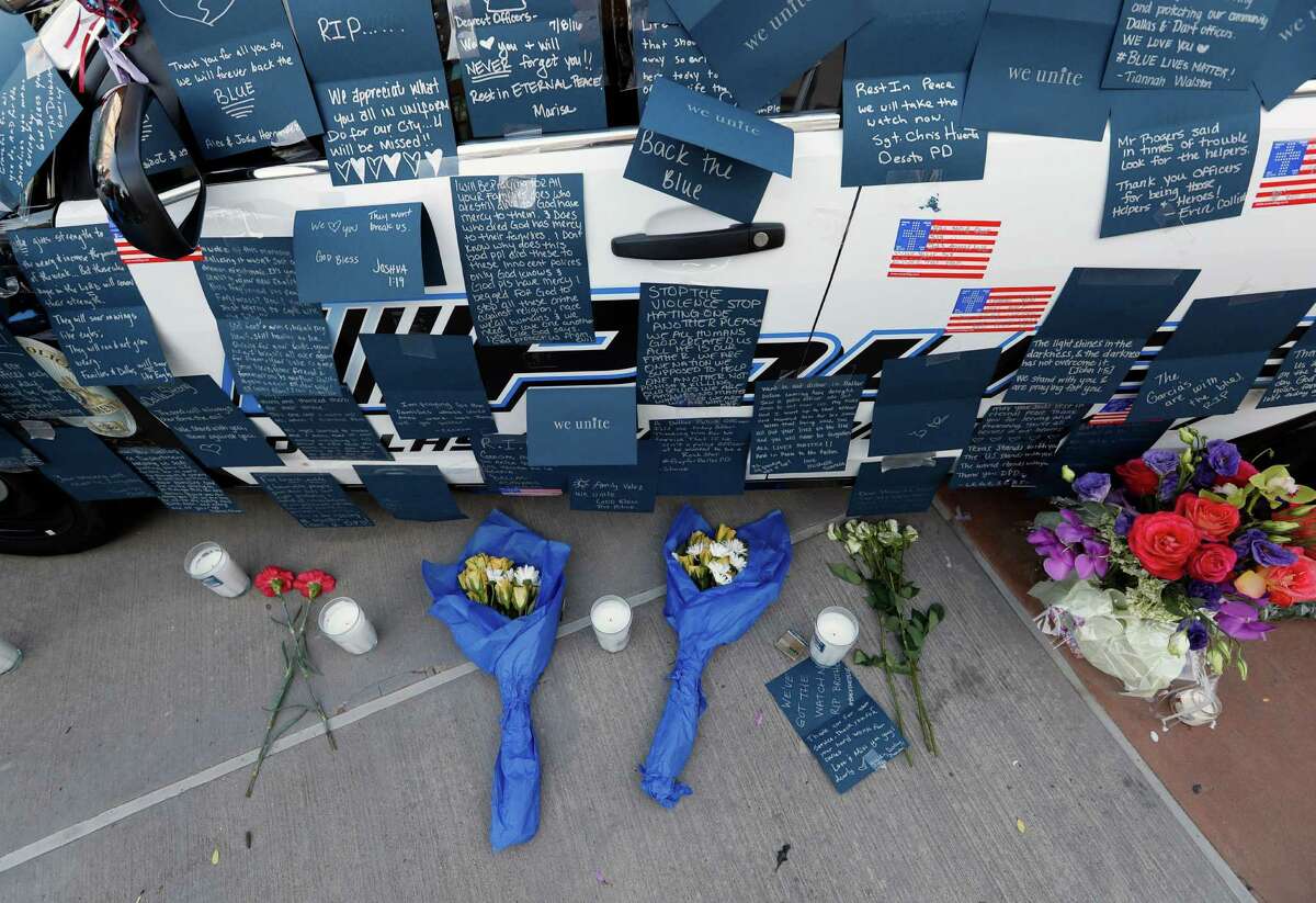 Notes, flowers and other items decorate a squad car at a make-shift memorial in front of the Dallas police department, Saturday, July 9, 2016, in Dallas.