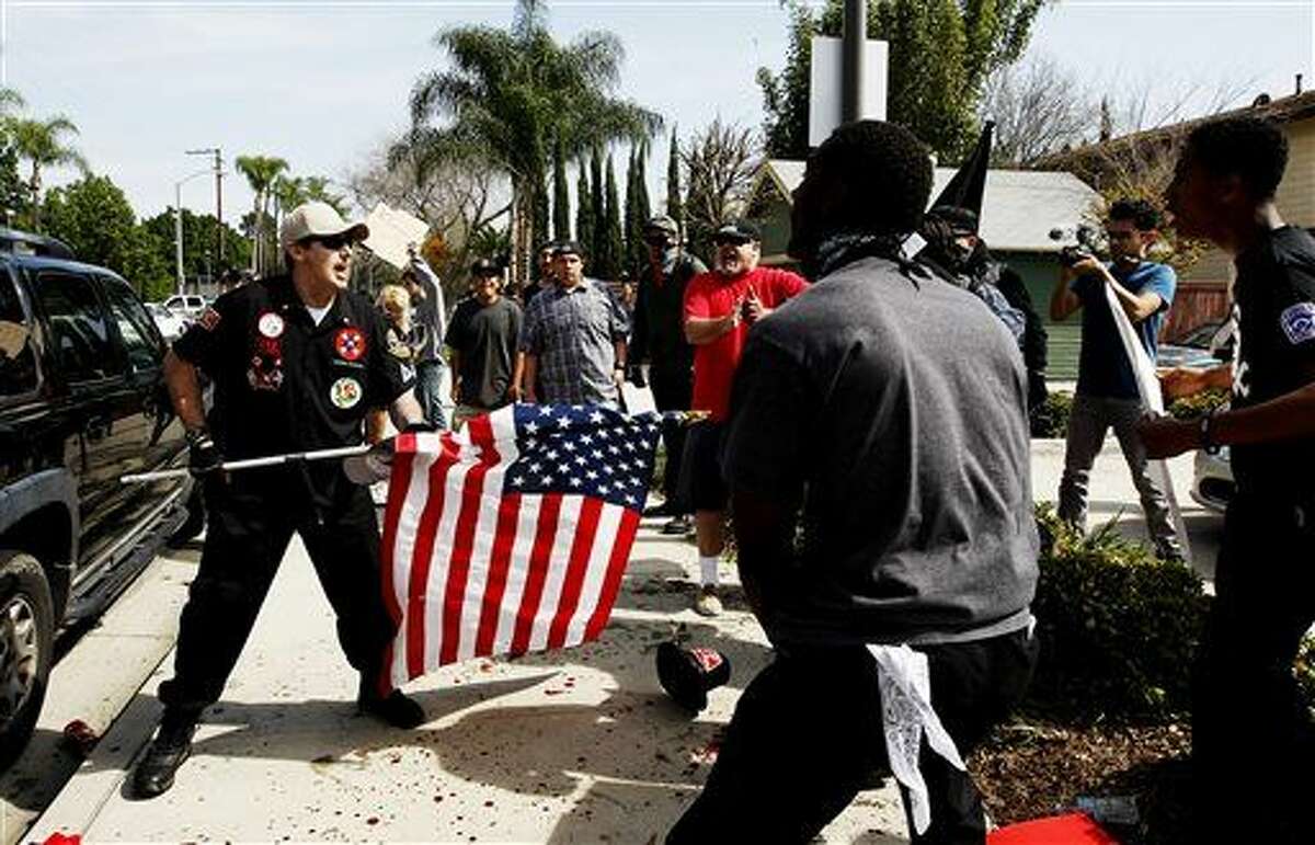 A Ku Klux Klansman, left, uses an American flag to fend off angry counter protesters after members of the KKK tried to start a "White Lives Matter" rally at Pearson Park in Anaheim, Calif., on Saturday, Feb. 27, 2016. The event quickly escalated into violence and at least two people had to be treated at the scene for stab wounds.