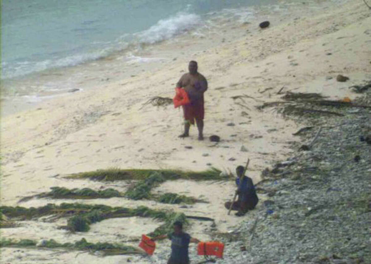 This photo provided by U.S. Navy released Thursday, April 7, 2016, shows a man waving a life jacket and two others looking on as a U.S. Navy P-8A maritime surveillance aircraft discovers them on the uninhabited island of Fanadik. The three men were back to safety on Thursday, three days after going missing. Officials say three men who had been missing for three days were rescued from a deserted Pacific island after a U.S. Navy plane spotted a gigantic "help" spelled out with palm leaves. (Ensign John Knight/U.S. Navy via AP)