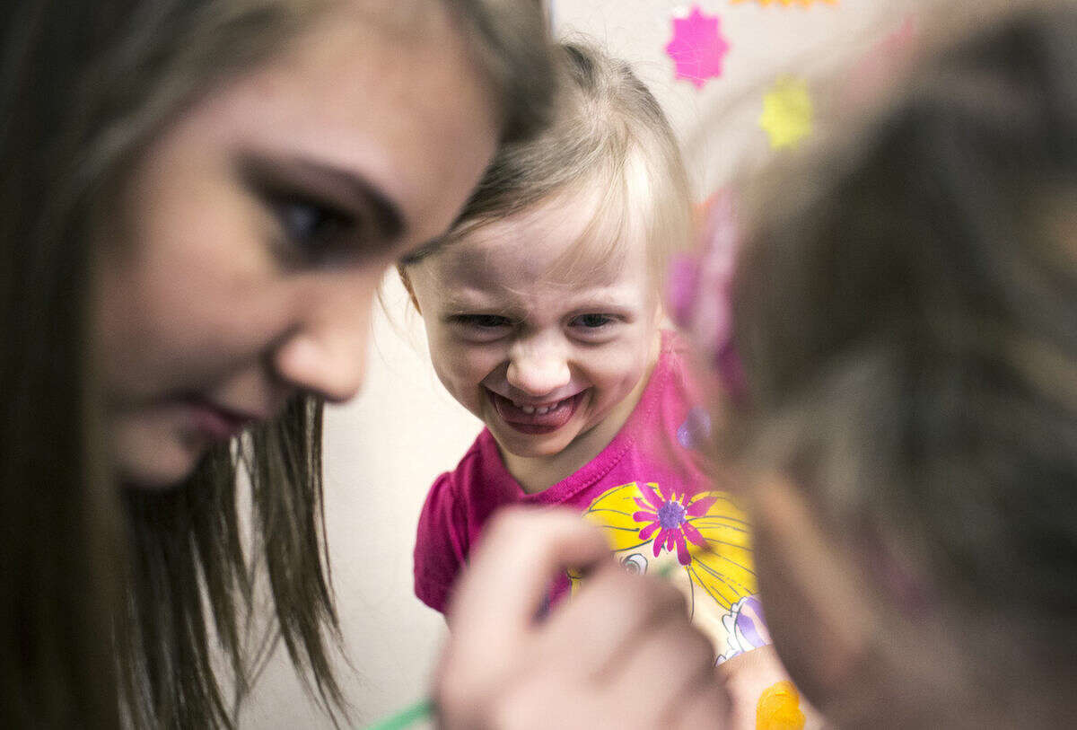 Lillian Duff, 4, of Midland, reacts while watching her sister, Catherine Duff, 2, right, have her face painted by volunteer Jade Sauve, 16, during the Trinity Lutheran Preschool's 50th anniversary celebration on Sunday.