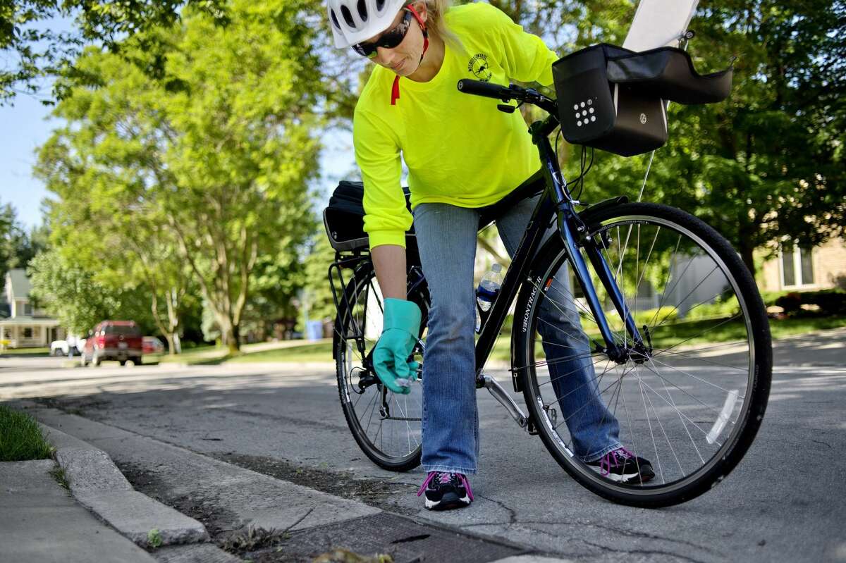 NICK KING | nking@mdn.net Midland County Mosquito Control employee Jessica Fetterman drops a mosquito growth regulator pellet into a water catch basin in Midland on Monday. Fetterman worked her route by bicycle as part of a pilot program.