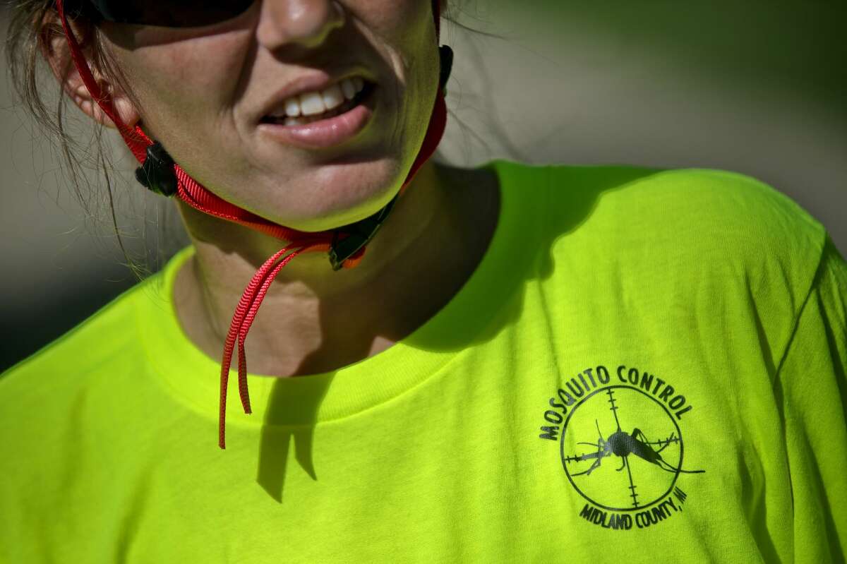 NICK KING | nking@mdn.net Midland County Mosquito Control employee Jessica Fetterman wears a bright green shirt with a Mosquito Control logo on the front and back to alert residents of her job duty while working her route by bicycle in Midland on Monday.