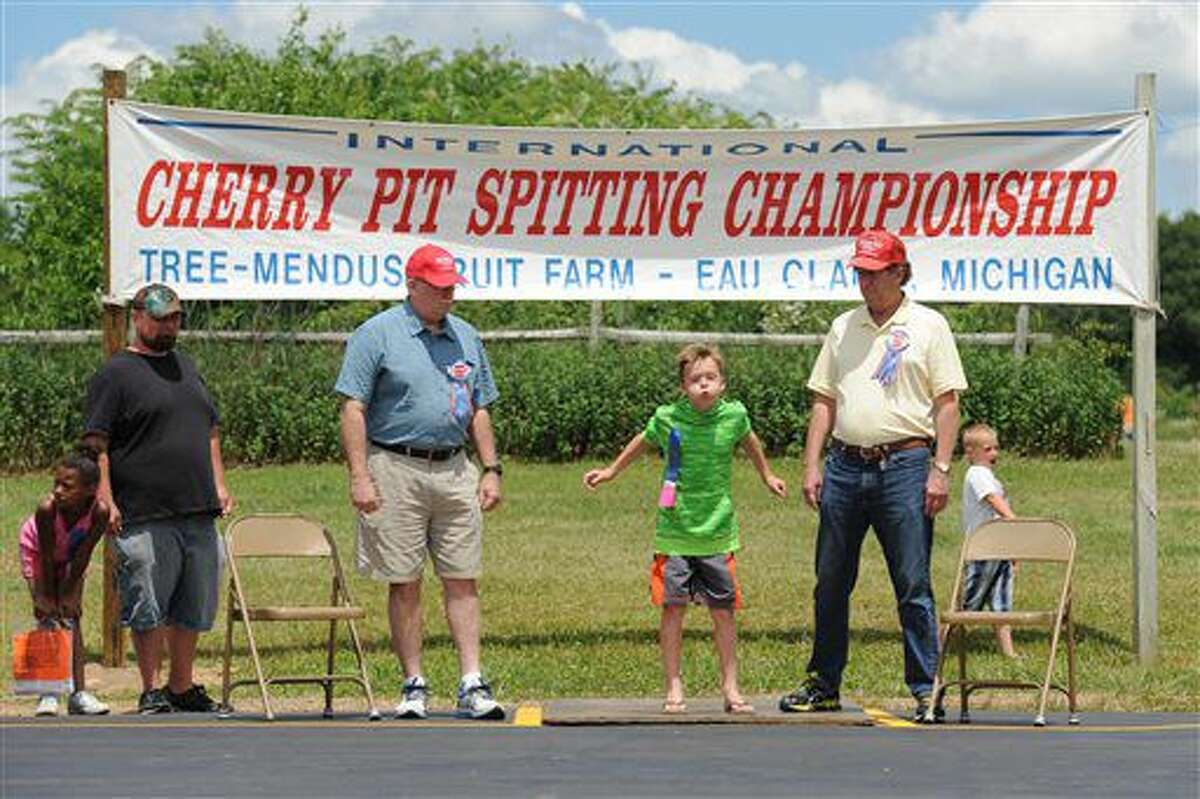 Reid Gillis, from Granger, Ind., is flanked by Berrien County Judge Sterling Schrock, left, and Berrien County Judge John Donahue during the 43rd International Cherry Pit-Spitting Championship Saturday, July 2, 2016, at Tree-Mendus Fruit Farm in Eau Claire, Mich. (Don Campbell/The Herald-Palladium via AP)