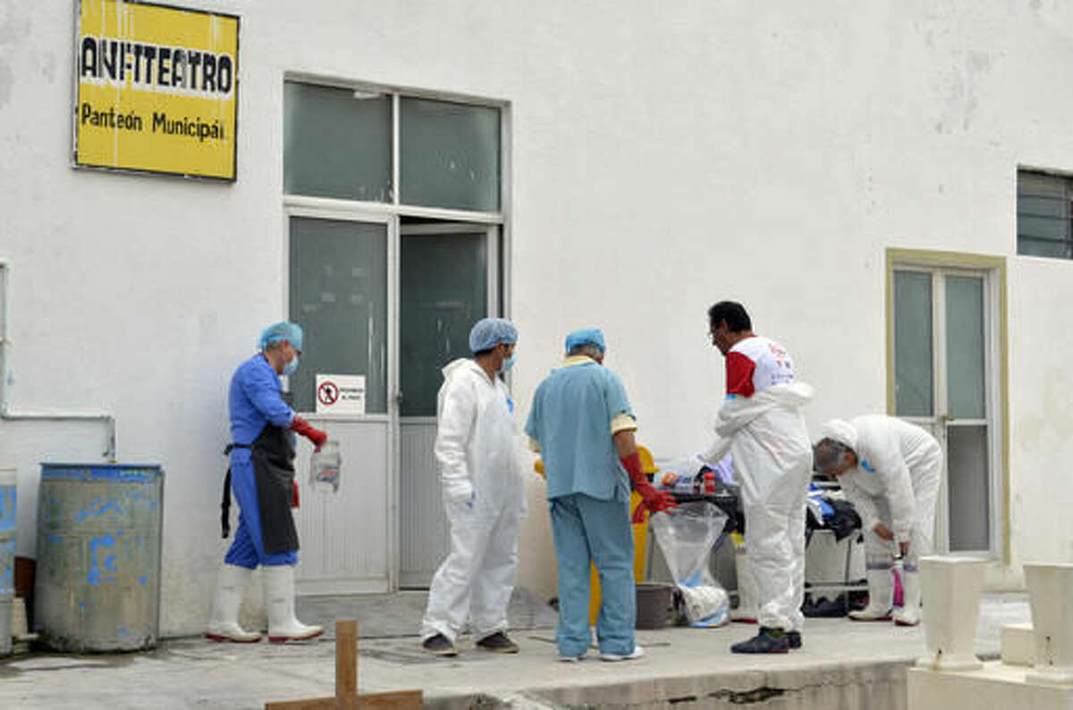 Forensic workers suit up as they continue the autopsies of 11 slain family members at a morgue inside the cemetery of the city of Tehuacan, Mexico, Saturda.