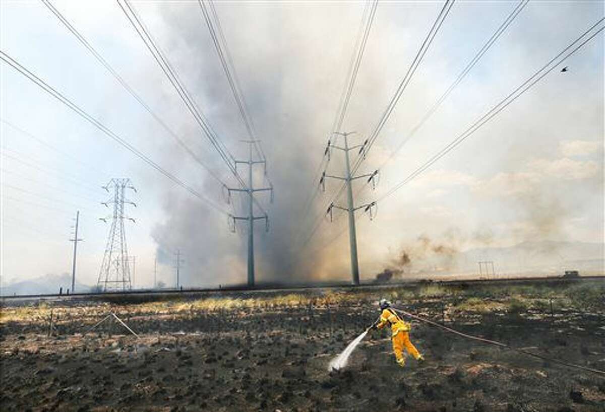 A Salt Lake City firefighter battle a grass fire along Instertate-80 that spread from a large fire at a commercial storage yard in Salt Lake City, Friday, July 8, 2016. (Jeffrey D. Allred/The Deseret News via AP)
