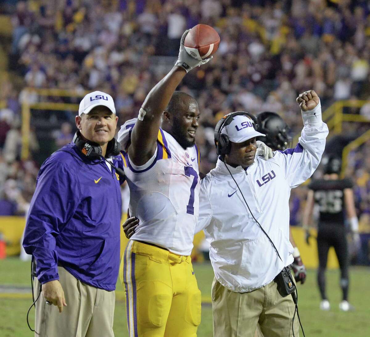 LSU running back Leonard Fournette holds the ball aloft after being recognized on the sideline for breaking the single-season rushing record, as he stands next to head coach Les Miles (left) and running backs coach Frank Wilson during in the second half against Texas A&M in Baton Rouge, La., on Nov. 28, 2015.