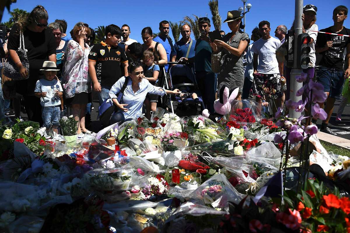 TOPSHOT - People lay flowers in the street of Nice to pay tribute to the victims the day after a gunman smashed a truck into a crowd of revellers celebrating Bastille Day, killing at least 84 people, on July 15, 2016. A Tunisian-born man zigzagged a truck through a crowd celebrating Bastille Day in the French city of Nice, killing at least 84 and injuring dozens of children in what President Francois Hollande on July 15 called a "terrorist" attack. / AFP PHOTO / ANNE-CHRISTINE POUJOULATANNE-CHRISTINE POUJOULAT/AFP/Getty Images