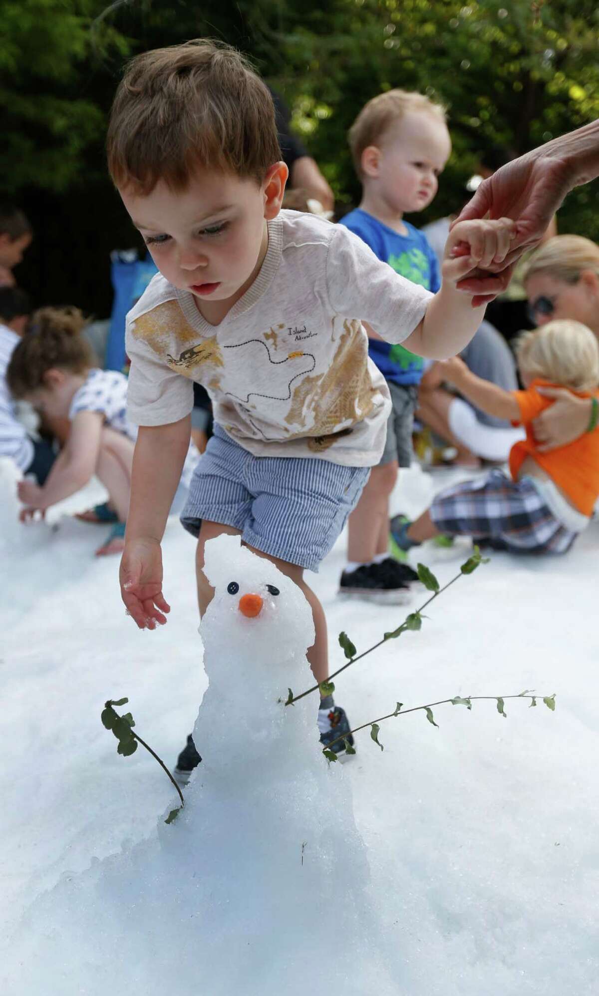 Grayson McMillian, 2 1/2, plays with his snowman in the ice during Snow Day at the Houston Zoo, Saturday, July 16, 2016, in Houston, provided by TXU Energy.