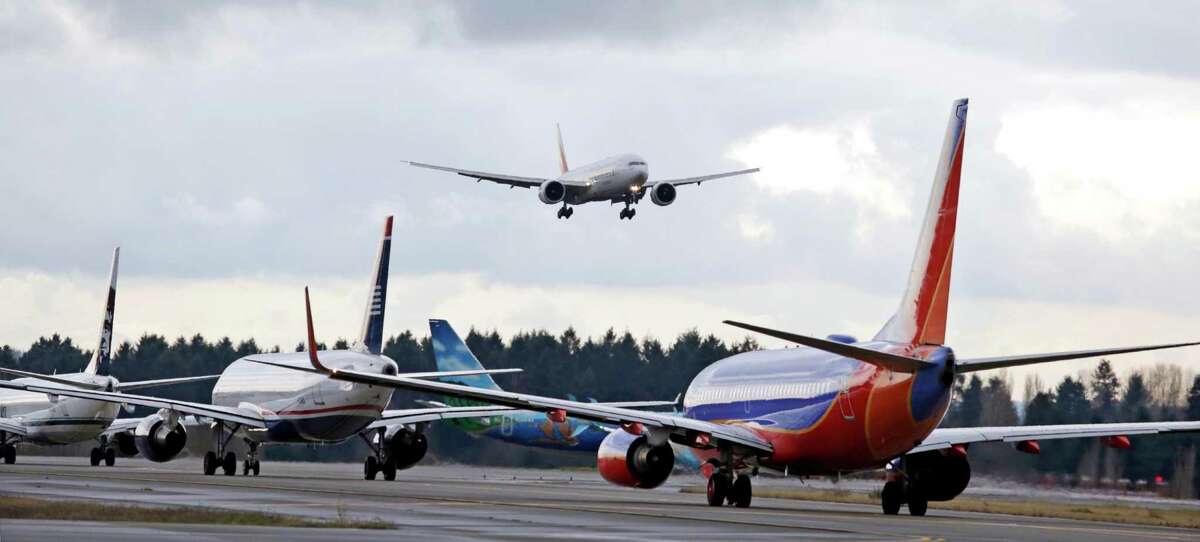 FILE - In this Dec. 16, 2015 file photo, a passenger jet comes in for a landing and in view of a line of planes waiting to takeoff, at Seattle-Tacoma International Airport. U.S. environmental regulators are moving to limit emissions from aircraft, ruling that jet engine exhaust is endangering human health by warming the planet. The Environmental Protection Agency announced Monday that it will use its authority under the Clean Air Act to regulate aircraft emissions. (AP Photo/Elaine Thompson)